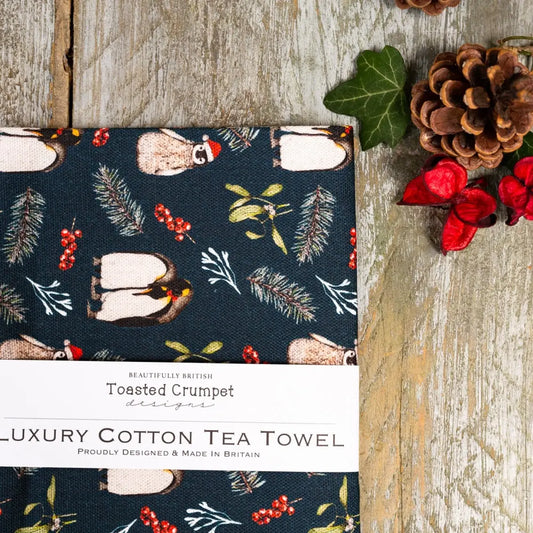 Luxury cotton tea towel with penguin design on a wooden surface with decorative elements.