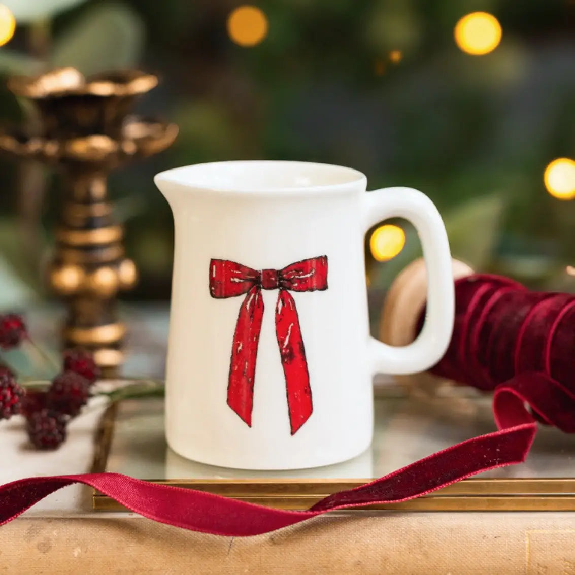 White mug with red bow design on a wooden surface with blurred Christmas lights in the background