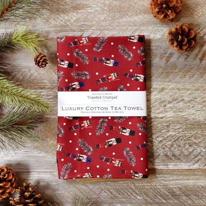 Red tea towel with Christmas pattern on a wooden surface with Nutcrackers,  pine cones and branches.