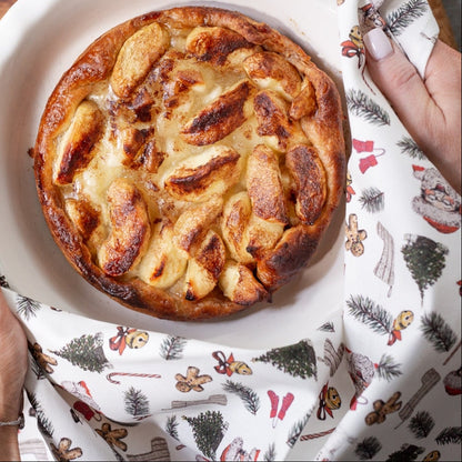 Apple pie in a white dish held by hands with a decorative cloth on a wooden table