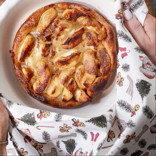 Apple pie in a white dish held by hands with a decorative cloth on a wooden table
