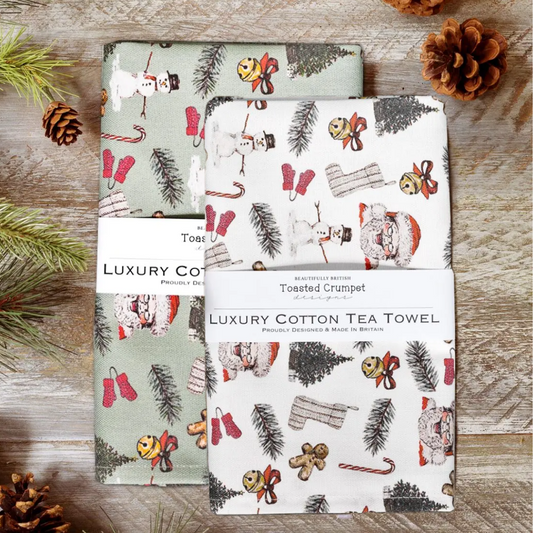 Two Christmas-themed tea towels on a wooden surface with pine cones.