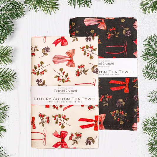 Two patterned tea towels with red bows and berries on a white and black background.