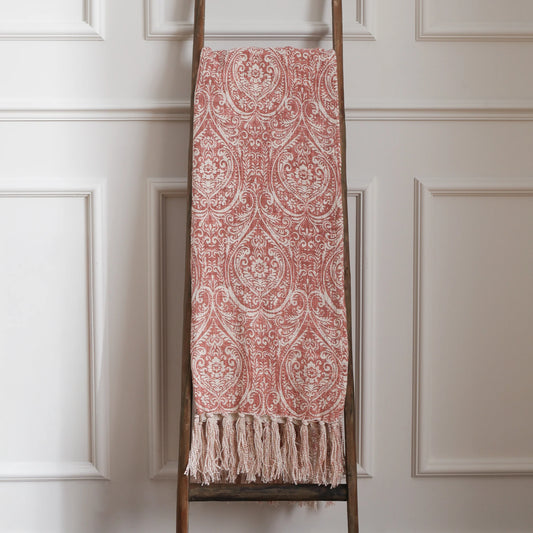 Decorative red and white damask patterned throw blanket on a wooden ladder against a white paneled wall.