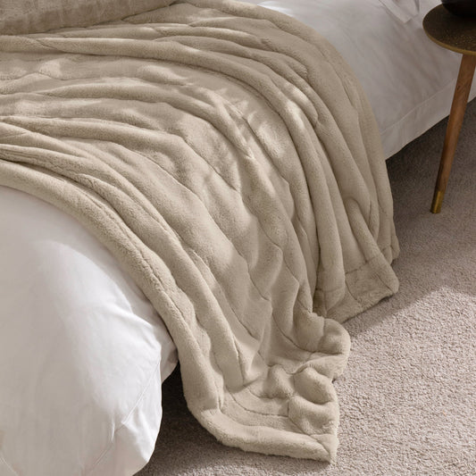 Beige faux fur throw draped over a bed in a bedroom setting