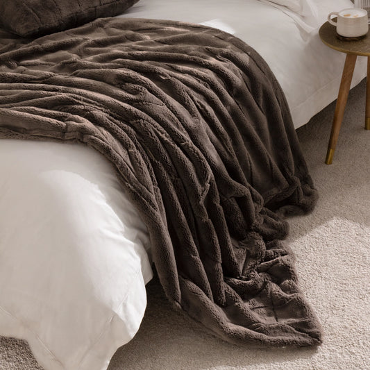 Brown textured faux fur throw draped over a bed with a side table in the background