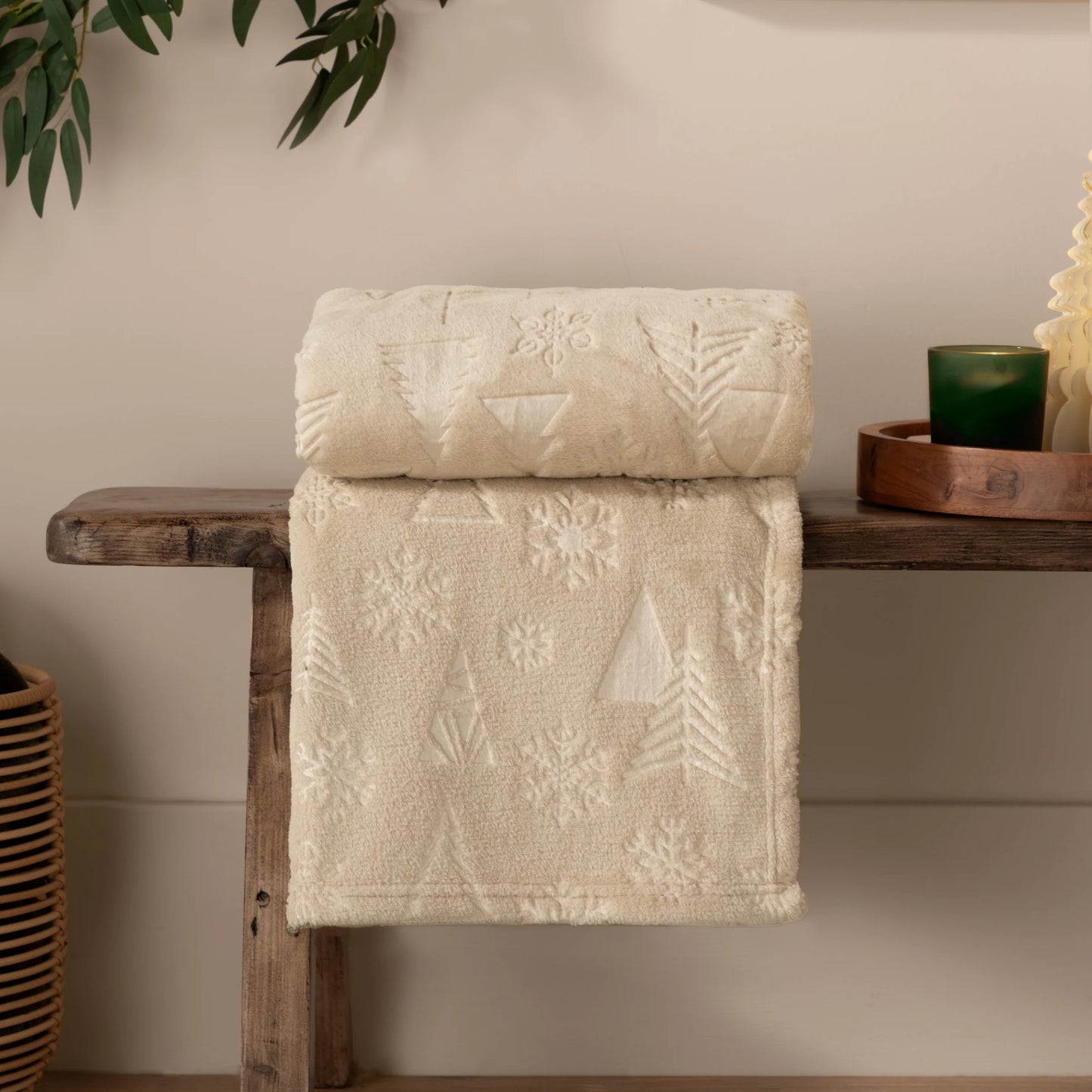 Beige textured throw with tree and snowflake patterns draped over a wooden shelf.