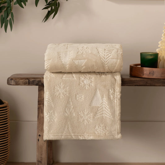 Beige textured throw with tree and snowflake patterns draped over a wooden shelf.