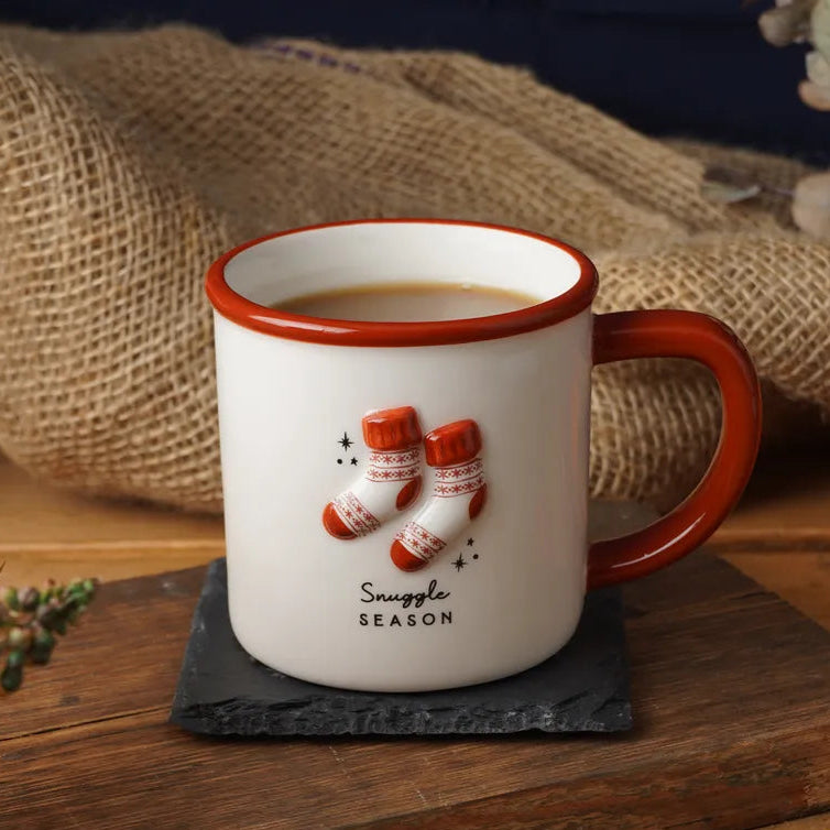 White mug with red rim and handle on a wooden surface with winter decorations