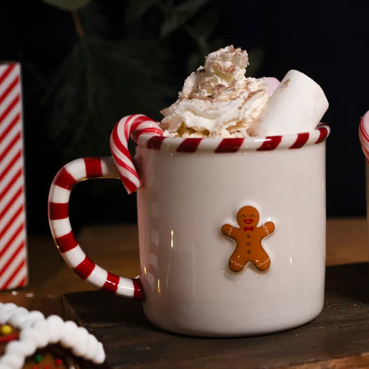 Two white mugs with candy cane handles, whipped cream, and gingerbread men on a wooden surface.
