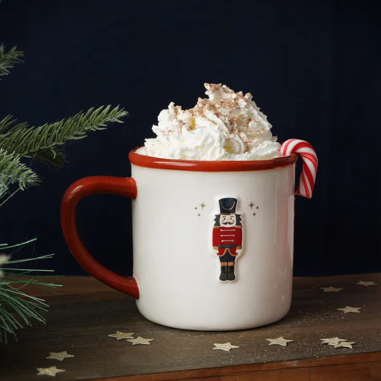 Mug with whipped cream and a candy cane on a festive table with Christmas decorations.