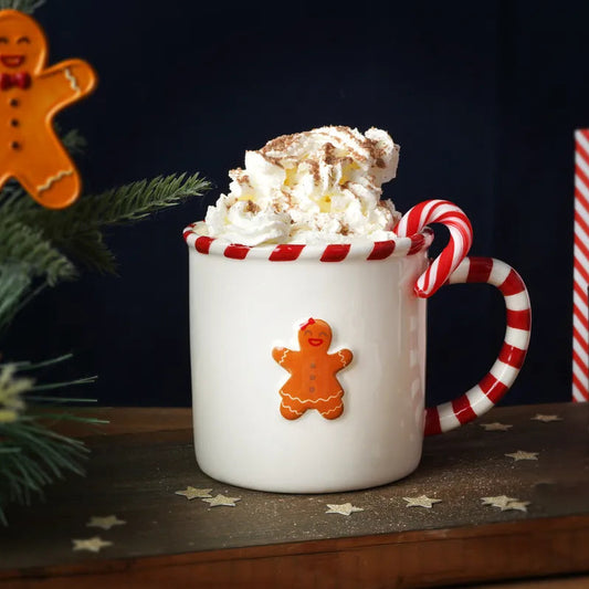 White mug with gingerbread design filled with hot chocolate, surrounded by Christmas decorations.