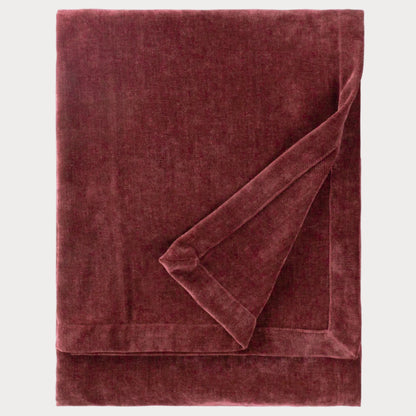 Folded burgundy velvet throw blanket on a white background