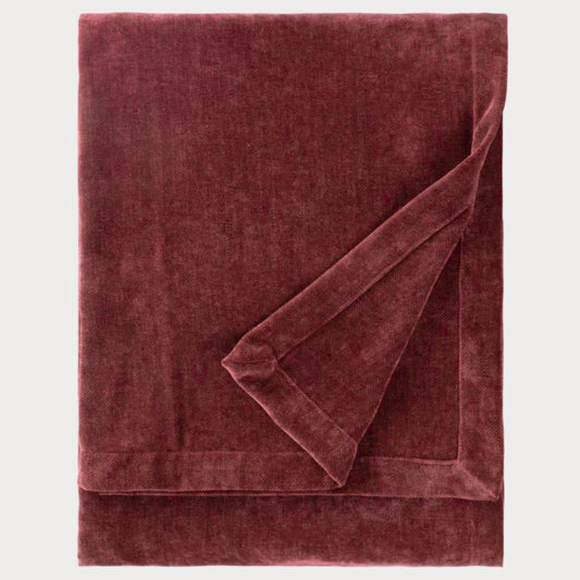 Folded burgundy velvet throw blanket on a white background