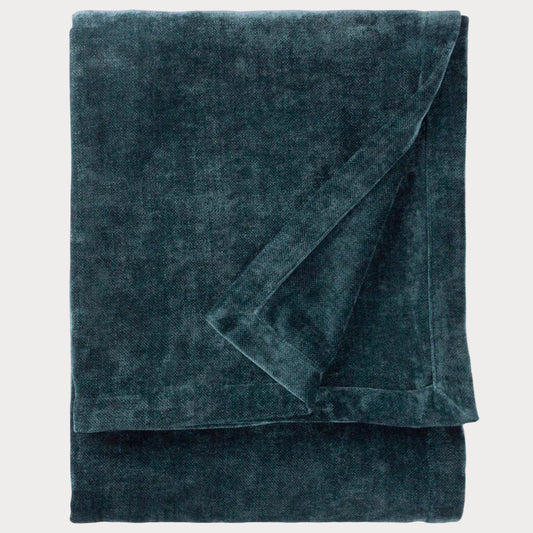 Folded dark teal throw on a white background