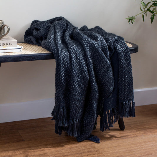 Navy blue knitted throw blanket draped over a wooden bench against a white wall.