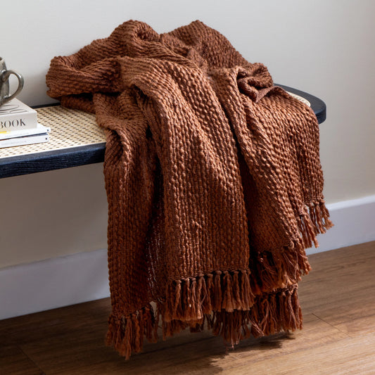 Brown textured blanket draped over a bench with a neutral background