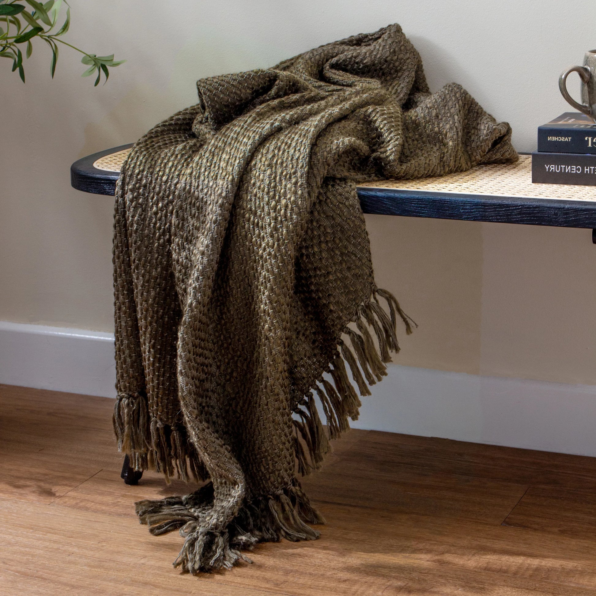 Brown-green textured throw blanket draped over a wooden table against a neutral wall.